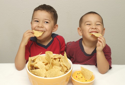 Two hispanic boys aged 4 and 5 years enjoying a bowl of tortilla chips with queso