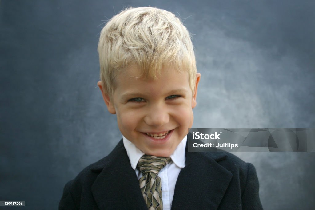 Blond grinning business boy Blond boy in business suit and tie with a mischievous grin centered on a gradient gray background Black Color Stock Photo