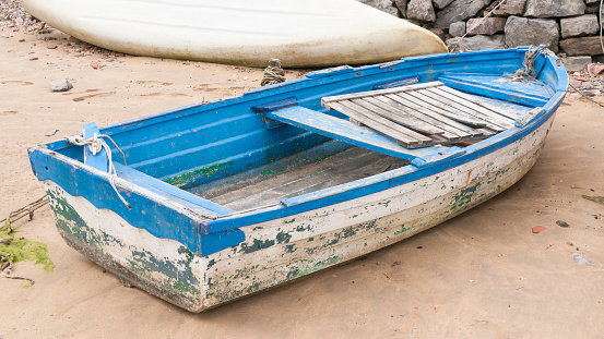 Weathered white and blue wooden boat in a sand beach
