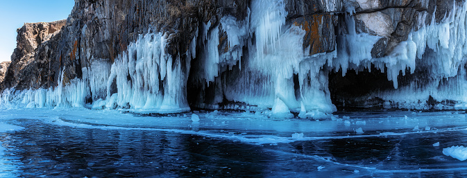 Beautiful winter panorama landscape with blue ice cave grotto and frozen clear icicles. Lake Baikal, Olkhon island, Russia. Natural winter background.