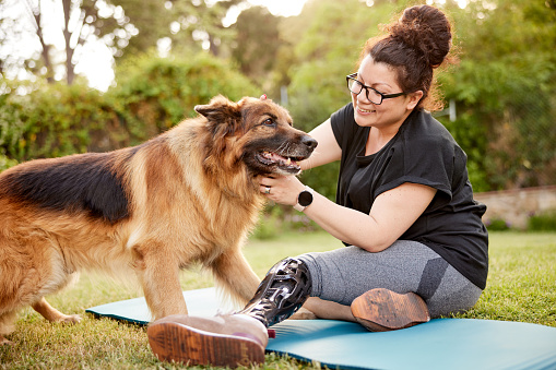 A woman is patting her dog on a yoga mat on a lawn.