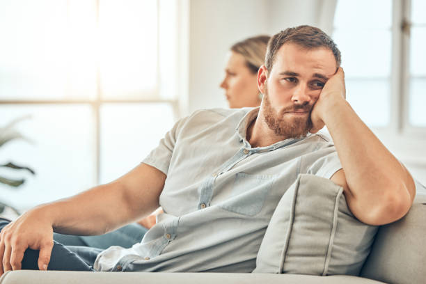 istock Young caucasian man with a beard looking unhappy and annoyed while sitting on the couch during an argument with his wife at home. Bored man sitting and thinking on the couch. 1399583010