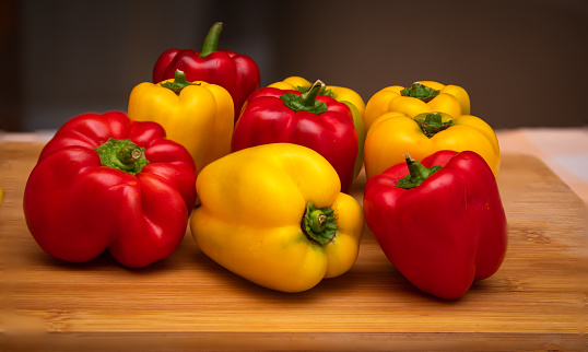 Close up of assorted red and yellow bell peppers placed on a cutting board in the kitchen. Also known as Sweet pepper, Pepper or Capsicum.