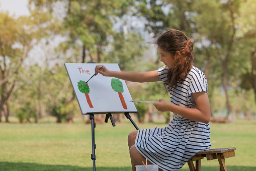 A young girl enjoys with water colors painting in the park.