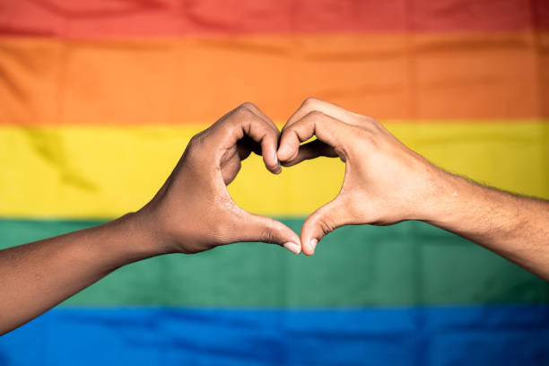 close up shot of hands making love or heart symbol in front of pride or rainbow flag - concept of gay couple love, solidarity and pride month celebration. - manifestação de paz imagens e fotografias de stock