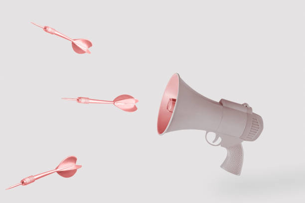 Copper arrows and beige gun-megaphone on isolated pastel background with copy space. Minimal abstract creative concept of hate, killing speech, fake news, hurtful words or warmongering rhetoric.