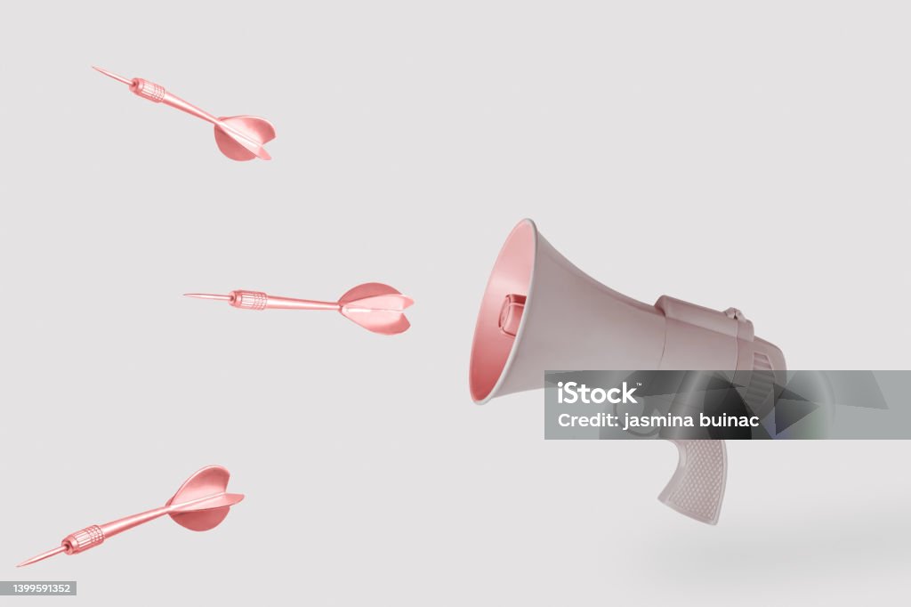 Copper arrows and beige gun-megaphone on isolated pastel background with copy space. Minimal abstract creative concept of hate, killing speech, fake news, hurtful words or warmongering rhetoric. Copper arrows and beige gun-megaphone on isolated pastel background with copy space. Minimal abstract creative concept of hate speech, killing speech, fake news, hurtful words, war propaganda or warmongering rhetoric. Concepts Stock Photo