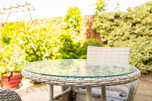 Shallow focus of the corner of a natural woven garden table, seen with its safety glass. Located on a patio area.