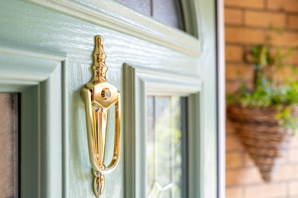 Shallow focus of a newly installed composite front door seen in a porch. The focus is on the brass door knocker with an internal peephole. key doormat stock pictures, royalty-free photos & images