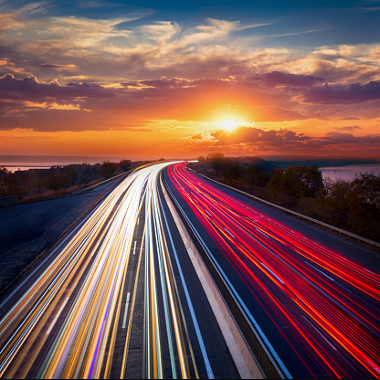 Light trails  lines of cars on the asphalt road. Sunset time with clouds and sun. Drive forward! Transport creative background. Long exposure, motion and blur.\