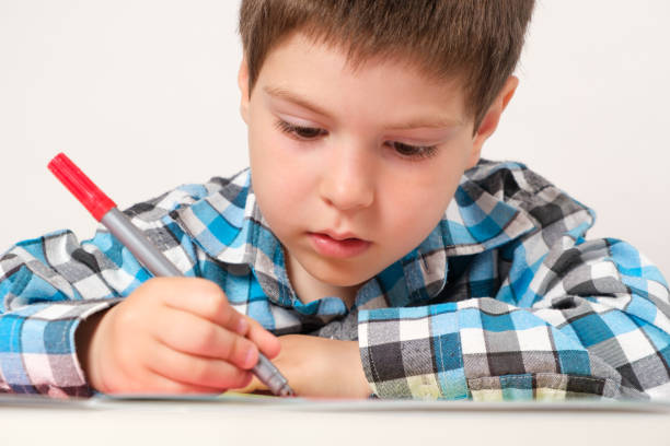 A 4-year-old boy draws with a felt-tip pen on paper, goes through labyrinths and interesting tasks to prepare for school