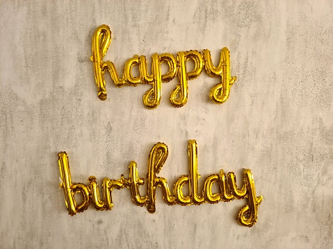 Happy Birthday balloon sign on a wall indoors.