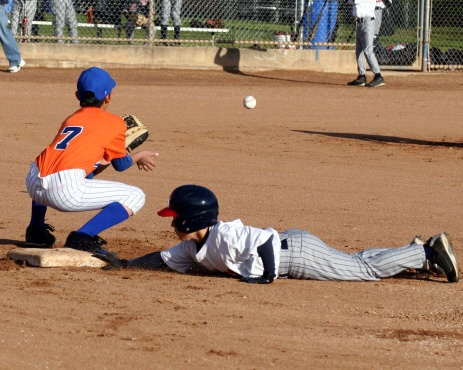 young boy baseball player dives back to first base