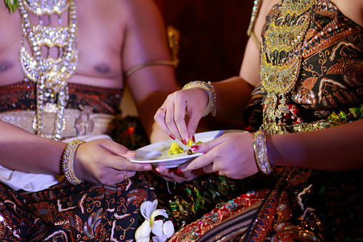 The hands of the Bridal Couple who will follow the ceremony feed each other in the tradition of Javanese marriage as an expression of mutual love.