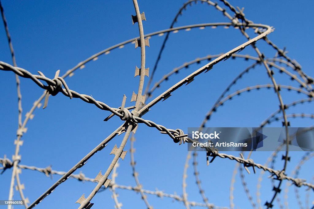 Close-up of a fence with barb wire Barb wire and razor wire fence against blue sky Crossing Stock Photo