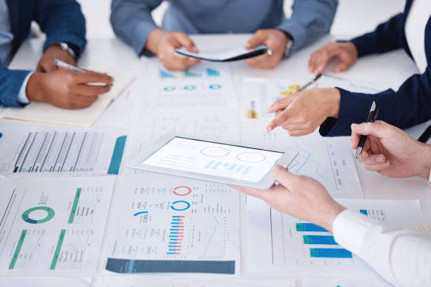 istock Unknown group of diverse businesspeople using a digital tablet during a boardroom meeting in an office. Closeup of colleagues planning and using paperwork and technology to brainstorm for strategy 1399605454