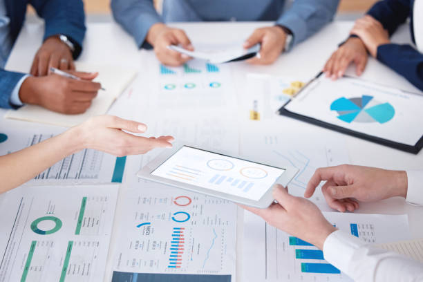 istock Unknown group of diverse businesspeople using a digital tablet during a boardroom meeting in an office. Closeup of colleagues planning and using paperwork and technology to brainstorm for strategy 1399605456