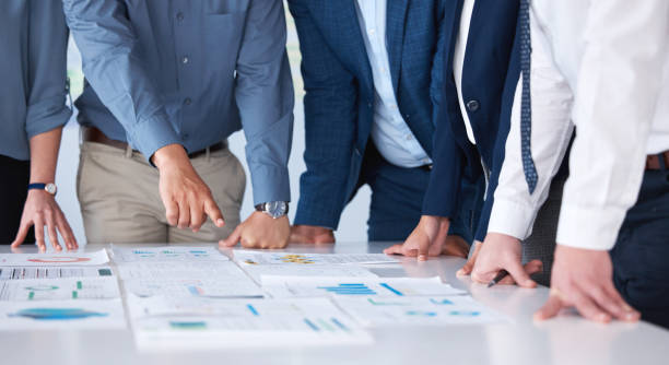 istock Unknown group of diverse businesspeople using paperwork during a boardroom meeting in an office. Closeup of colleagues standing and planning while using documents to brainstorm a strategy together 1399605458