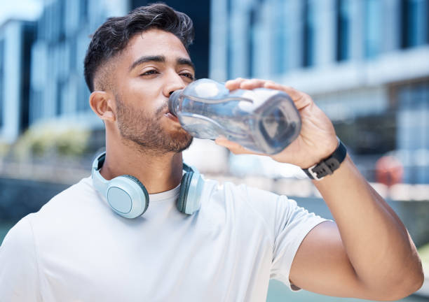 istock Young male athlete taking a break while drinking water from a bottle and wearing his headphones around his neck while out for a run and exercising outdoors during the day 1399607542
