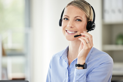 Portrait of young caucasian female call centre agent talking on headset while working on computer in an office. Confident and happy businesswoman consulting and operating a helpdesk for customer sales and service support