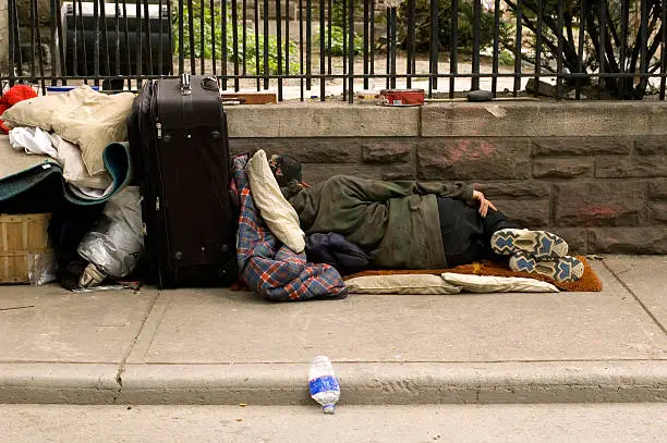 Homeless person sleeping on the sidewalk with bags.