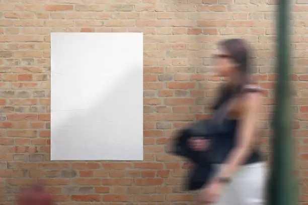 Photo of Blank white crumpled poster on street brick wall. Young woman passing