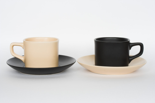 Two coffee cups opposite each other - beige and black, with changed saucers, isolated on white