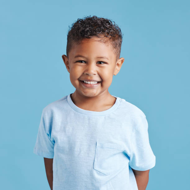 카메라를 바라보고 있는 미소 짓는 작은 갈색 머리 소년의 초상화. 파란색 배경에 치과를위한 건강한 치아를 가진 행복한 아이 - 아이 이미지 뉴스 사진 이미지