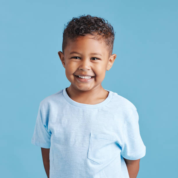 Portrait of a smiling little brown haired boy looking at the camera. Happy kid with good healthy teeth for dental on blue background Portrait of a smiling little brown haired boy looking at the camera. Happy kid with good healthy teeth for dental on blue background innocence stock pictures, royalty-free photos & images