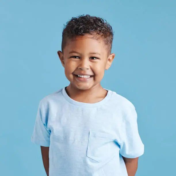Portrait of a smiling little brown haired boy looking at the camera. Happy kid with good healthy teeth for dental on blue background