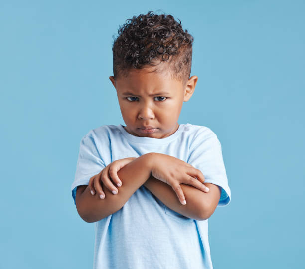 istock Offended little hispanic boy looking sad and upset while standing against a blue studio background. Unhappy preschooler standing with his arms crossed and looking down 1399611785