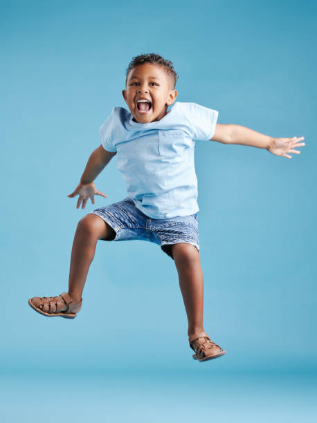 glücklicher junger entzückender kleiner hispanischer junge, der in die luft springt, isoliert auf blauem hintergrund. lustiges vorschulkind, das seine aufregung ausdrückt und spaß hat - child lifestyles isolated blue stock-fotos und bilder