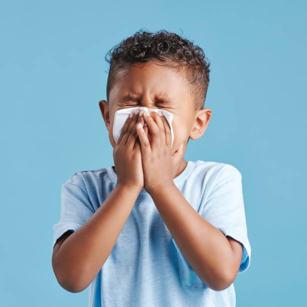 istock Little hispanic boy blowing his nose with tissue against blue studio background. Child feeling sick with flu virus or infection and suffering with snotty nose 1399611807