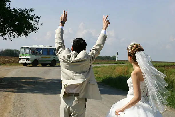 Photo of Just married couple hitchhiking in a field