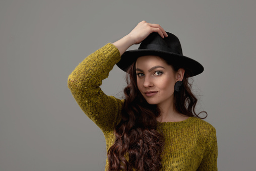 close-up portrait of a beautiful and positive young girl in a black hat, isolated on gray background