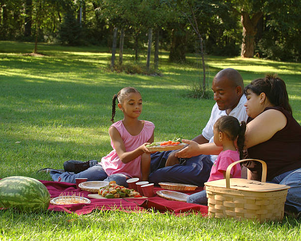 Interracial Family Picnic African American Dad, Hispanic Mom and 2 daughters picnicing in a park. black man eating watermelon stock pictures, royalty-free photos & images