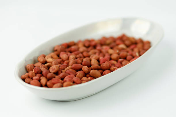 Stock photo features a pile of dried redskin peanuts with their skin intact, set against a white background. These peanuts are rich in protein and dietary fiber, making them a nutritious snack. Their crunchy texture and robust flavor make them ideal for roasting, seasoning, or adding to a variety of dishes for enhanced taste and nutrition.