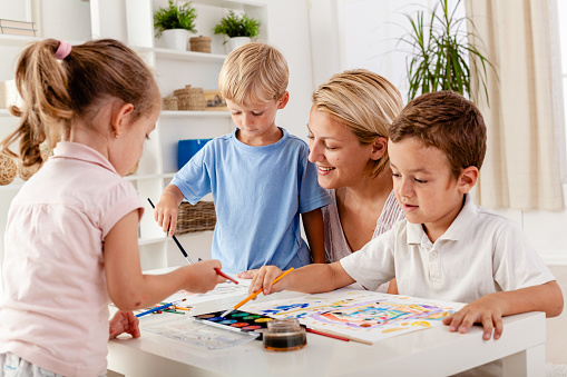 Mother having fun with her children painting with watercolors at home