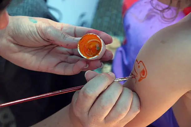 A dog tattoo being hand-painted on the shoulder of a kid