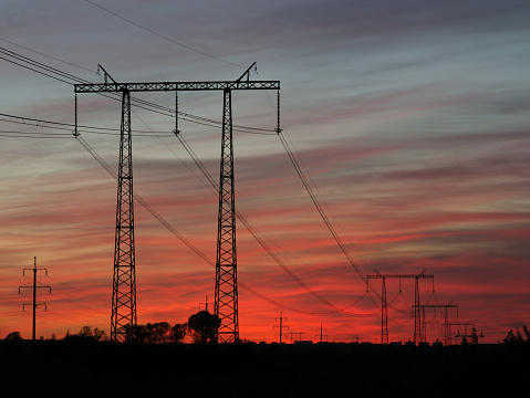 Silhouette of electric transmission line against sunset sky.