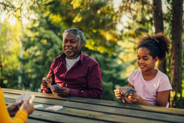 Grandparents playing cards with their grandchild Teenage afro girl playing cards while sitting in in the backyard with senior grandparents family playing card game stock pictures, royalty-free photos & images