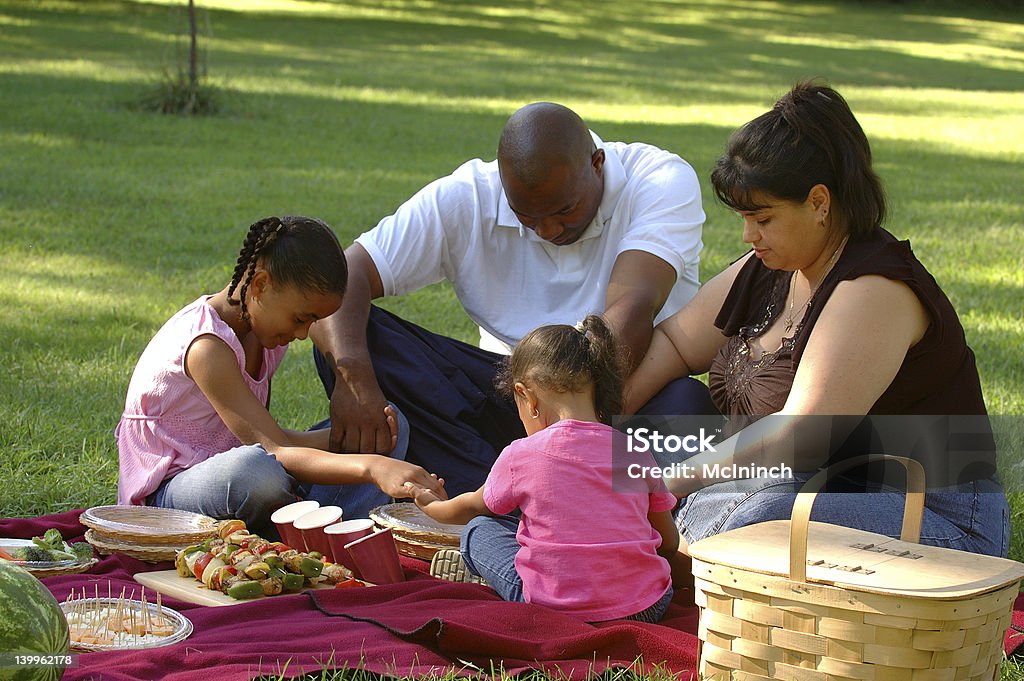Picnicking family saying grace Interracial family saying grace around picnic blanket Praying Stock Photo