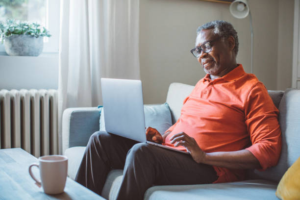 Mature man using laptop Mature man at home, sitting on sofa and using laptop. one man only stock pictures, royalty-free photos & images