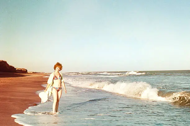 Vintage image of a woman in a bikini walking by the sea and smiling at the camera. Vintage image from the seventies.