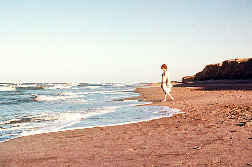 Vintage image of a woman walking by the sea on an isolated beach. Vintage photo from the seventies of the 20th century.