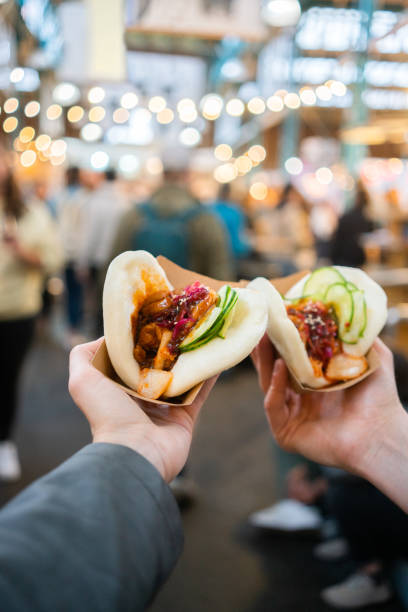 Personal perspective shot of a couple eating street food at a festival Personal perspective shot of a couple eating bao  sandwiches at a food festival night market stock pictures, royalty-free photos & images