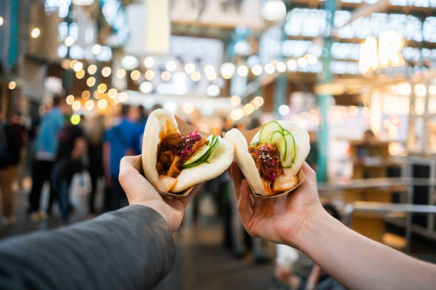 Personal perspective shot of a couple eating street food at a festival Personal perspective shot of a couple eating bao  sandwiches at a food festival food festival stock pictures, royalty-free photos & images