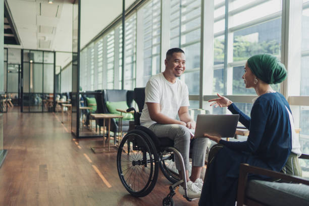 Teamwork in business - A female leader sharing insights with a disabled co worker Teamwork in business - A female leader sharing insights with a disabled co worker wheelchair stock pictures, royalty-free photos & images