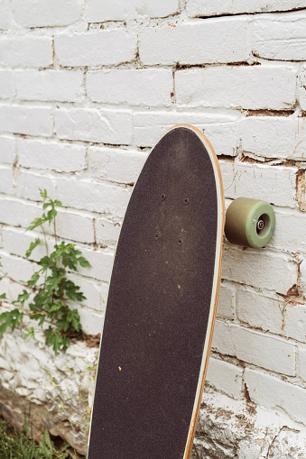 Skateboard against a white brick wall with light foliage.