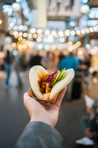 Personal perspective shot of a woman's hand holding a bao bun with tofu at a street market
